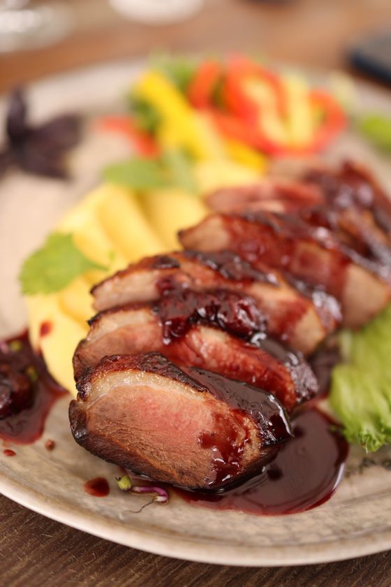 Sliced pink duck breast glazed with dark cherry sauce beside mango slices, peppers and lettuce