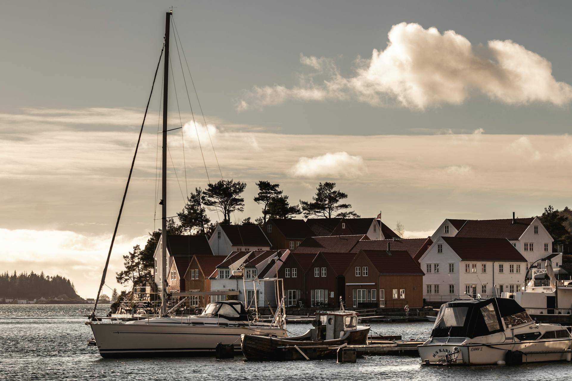 Picturesque harbor view in Norway with sailboats and charming coastal houses at sunset.