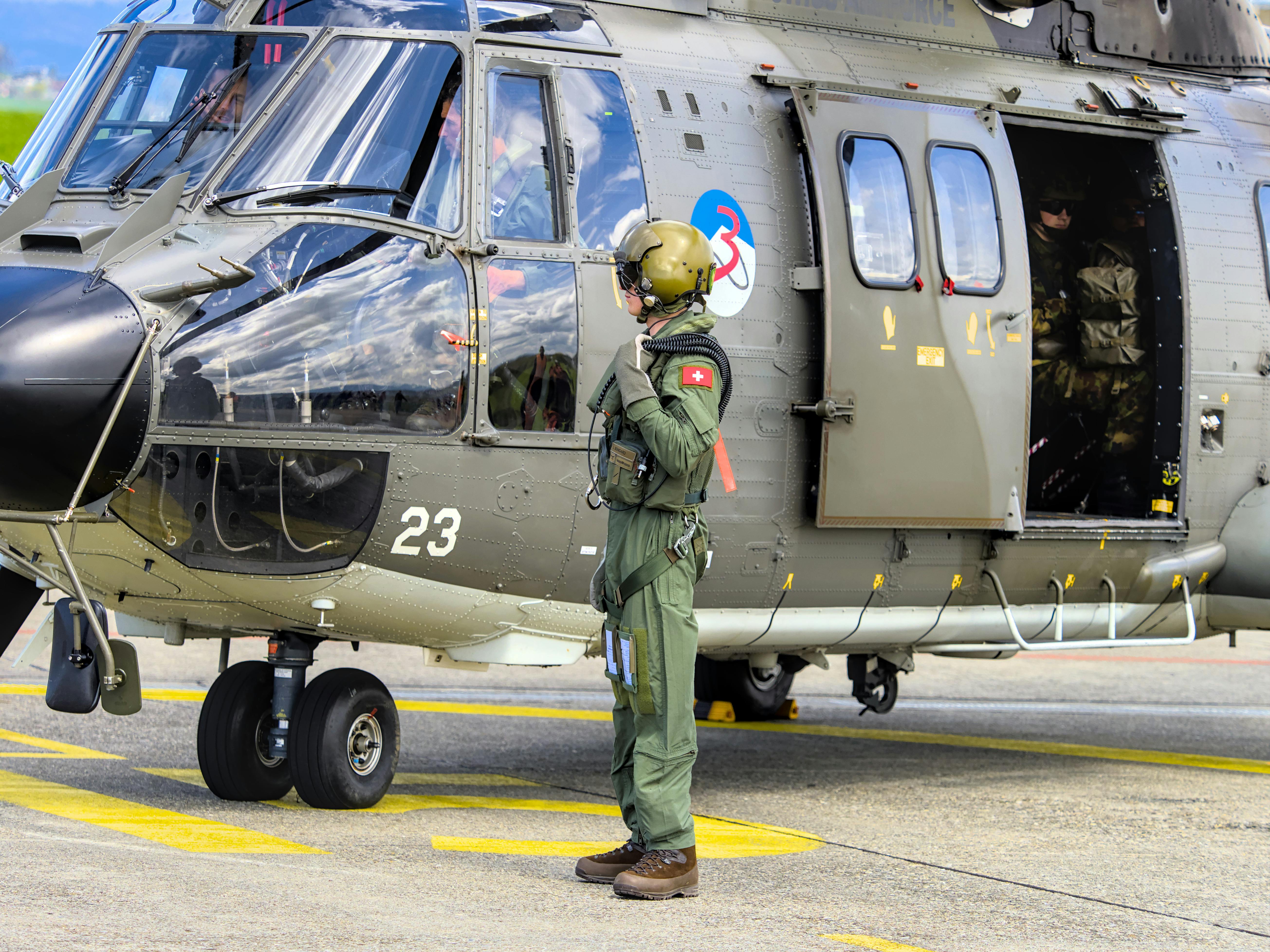 Swiss soldier stands next to military helicopter at Payerne airfield. Aviation and defense theme.