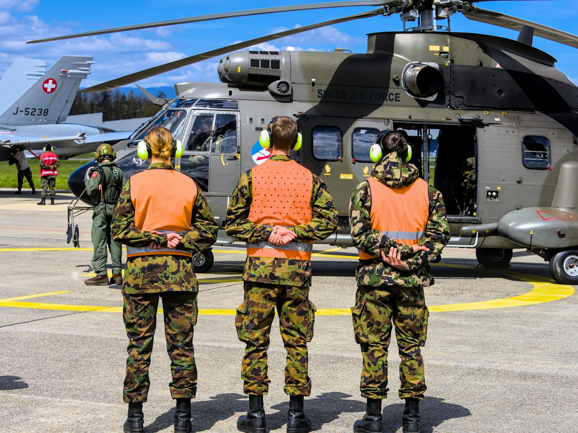 Swiss Air Force personnel in uniform at Payerne base, standing by a military helicopter.