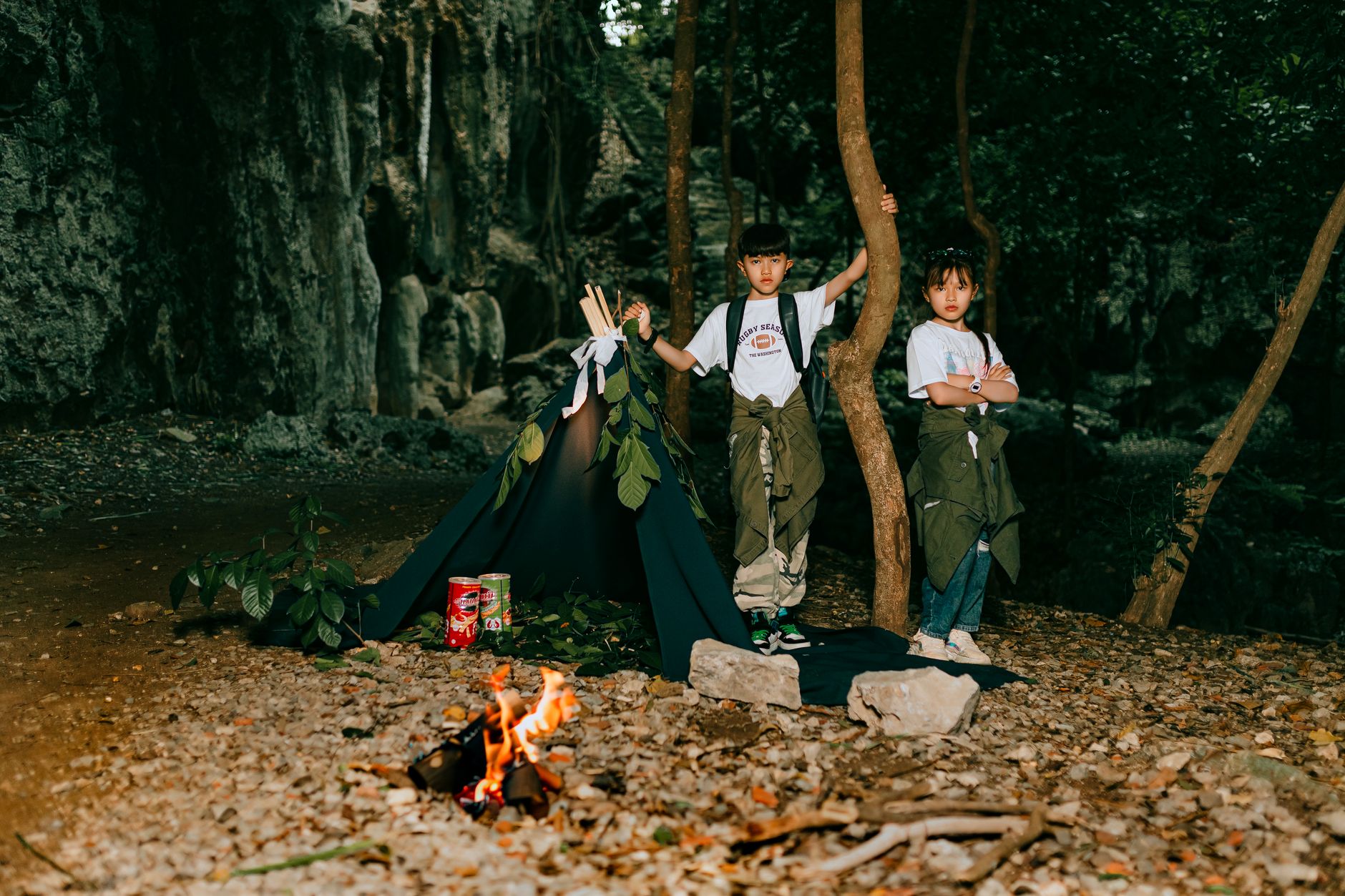 Two kids enjoying a camping adventure in the forest with a small campfire and tent.