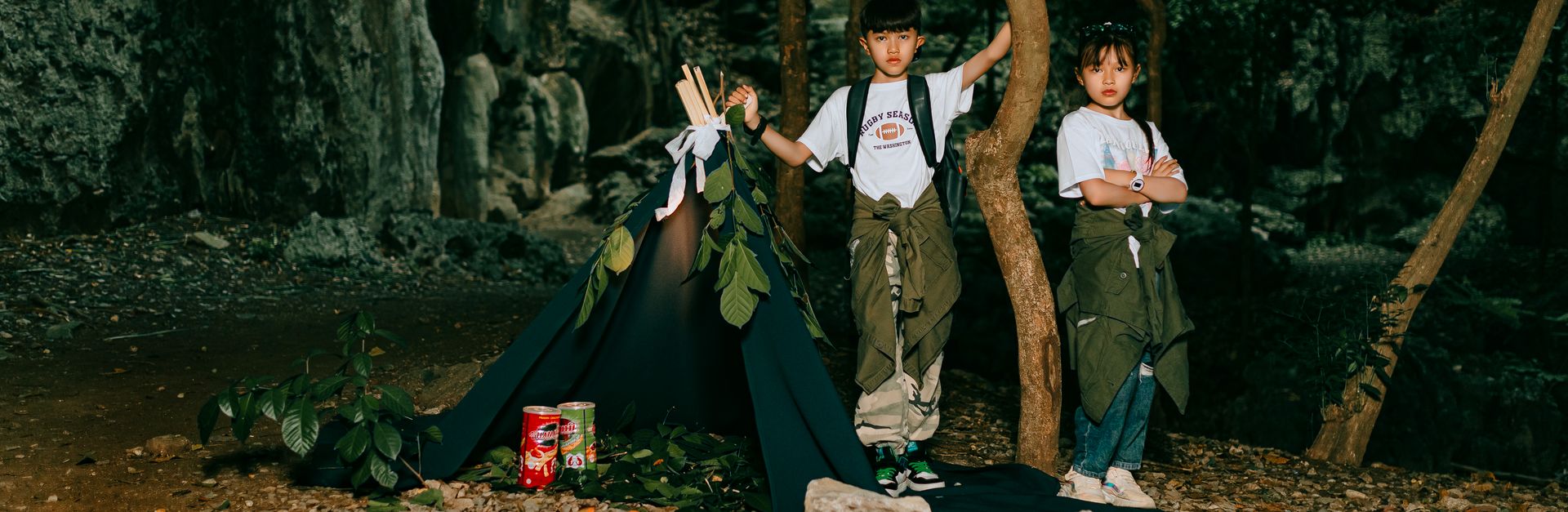 Two kids enjoying a camping adventure in the forest with a small campfire and tent.