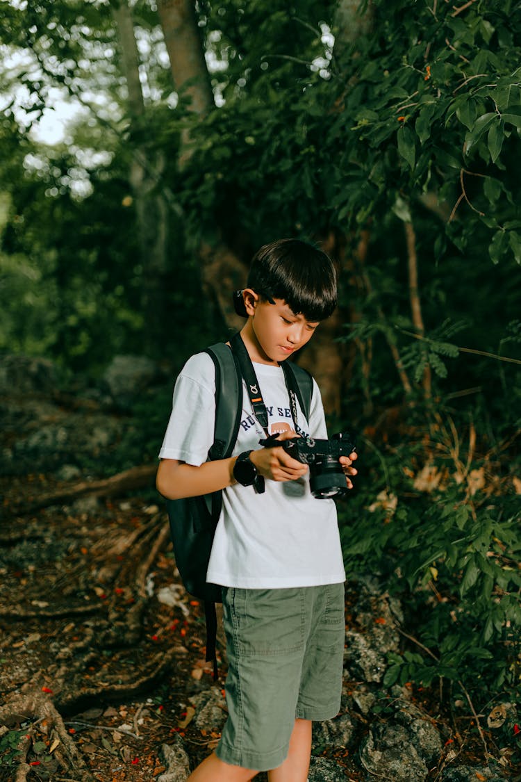 A Boy Standing In A Forest And Looking At The Pictures In The Camera Viewfinder 