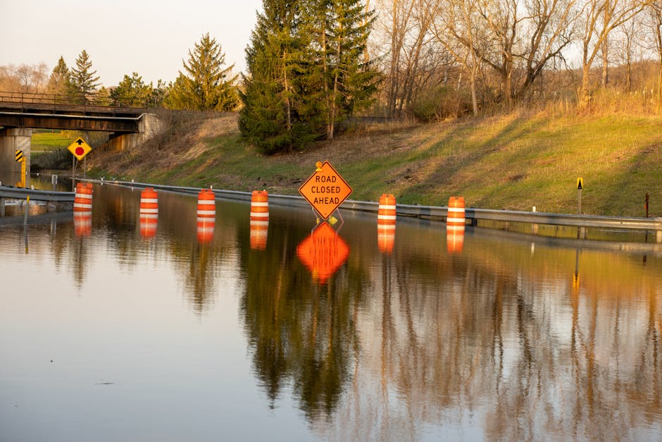 Photo by Tom Fisk A flooded road with warning signs indicating 'Road Closed Ahead' due to water overflow.