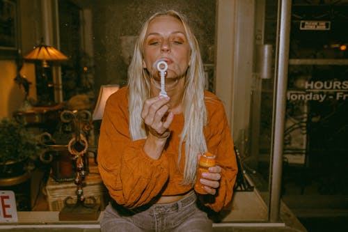 Woman in Orange Blouse Blowing Soap Bubbles