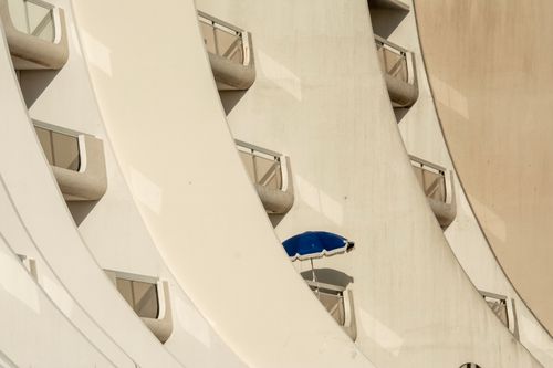 Free A modern building facade with curved balconies and a blue umbrella, sunlit and urban. Stock Photo