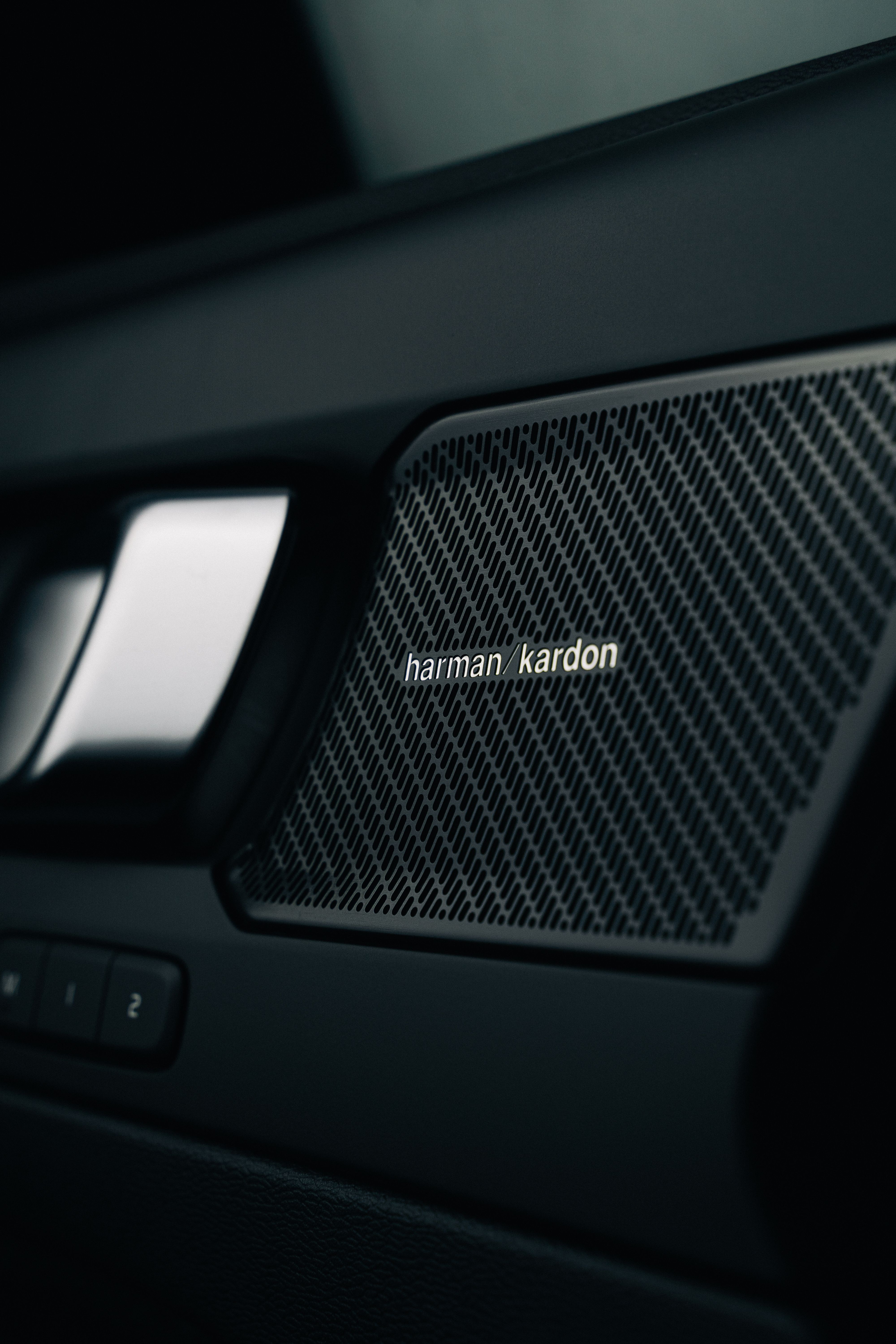 Detailed close-up of a Harman Kardon speaker grille in a modern car interior showcasing advanced audio technology.