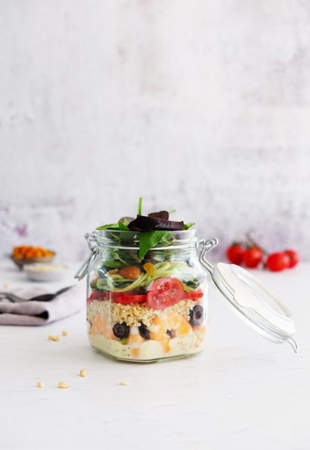 Vibrant layered salad in a glass jar with fresh vegetables on a clean white background.