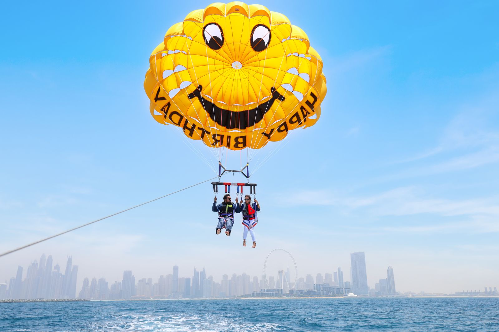 Couple parasailing over Dubai's coast with the city skyline and sea behind them