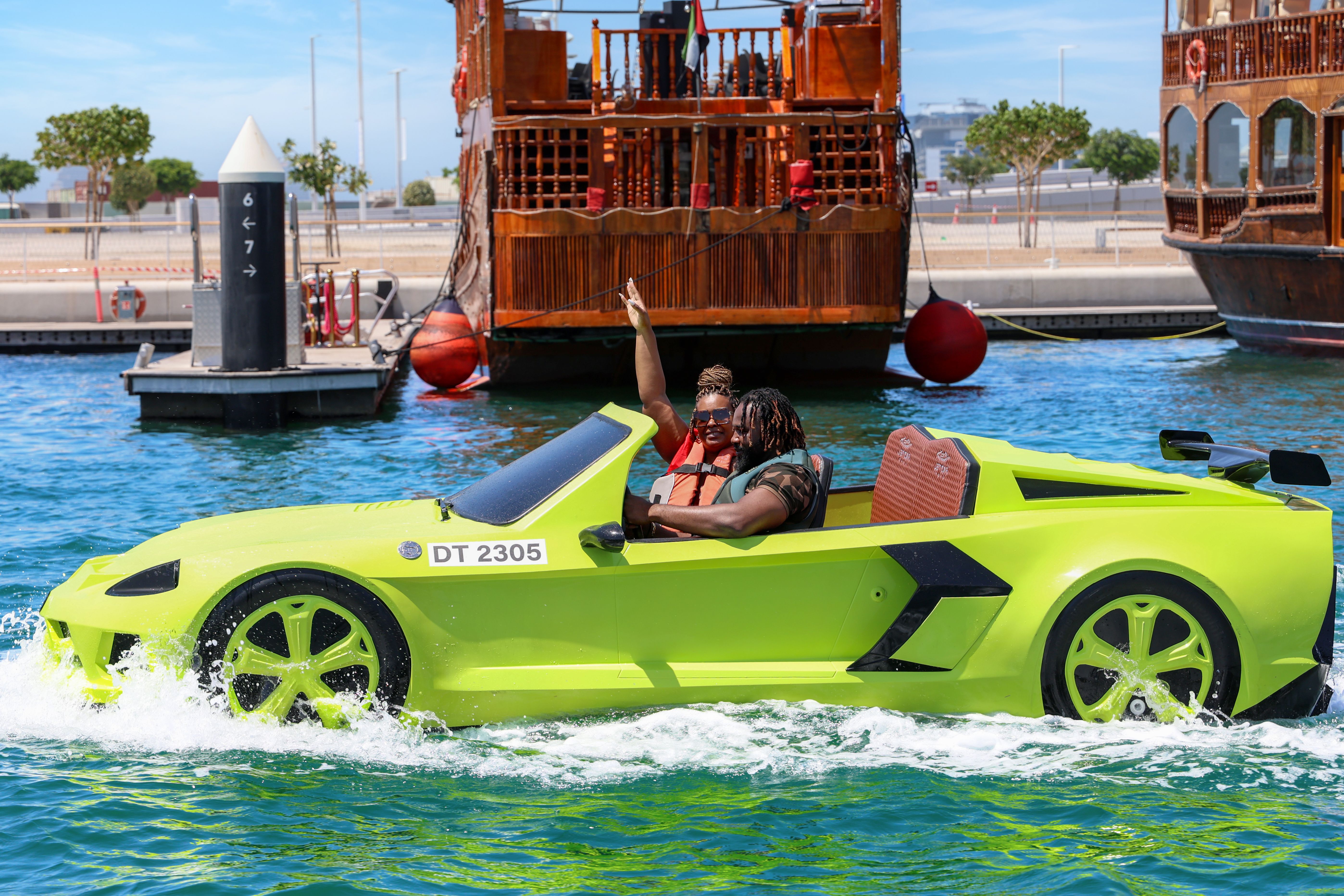 A joyful couple rides an amphibious car on the blue waters of Dubai, capturing adventurous fun.