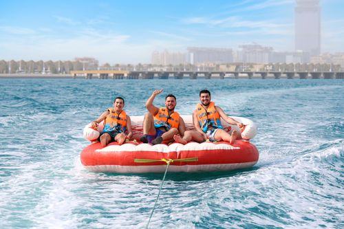 Free Three men on an inflatable tube enjoying a thrilling water adventure in Dubai, wearing life vests for safety. Stock Photo