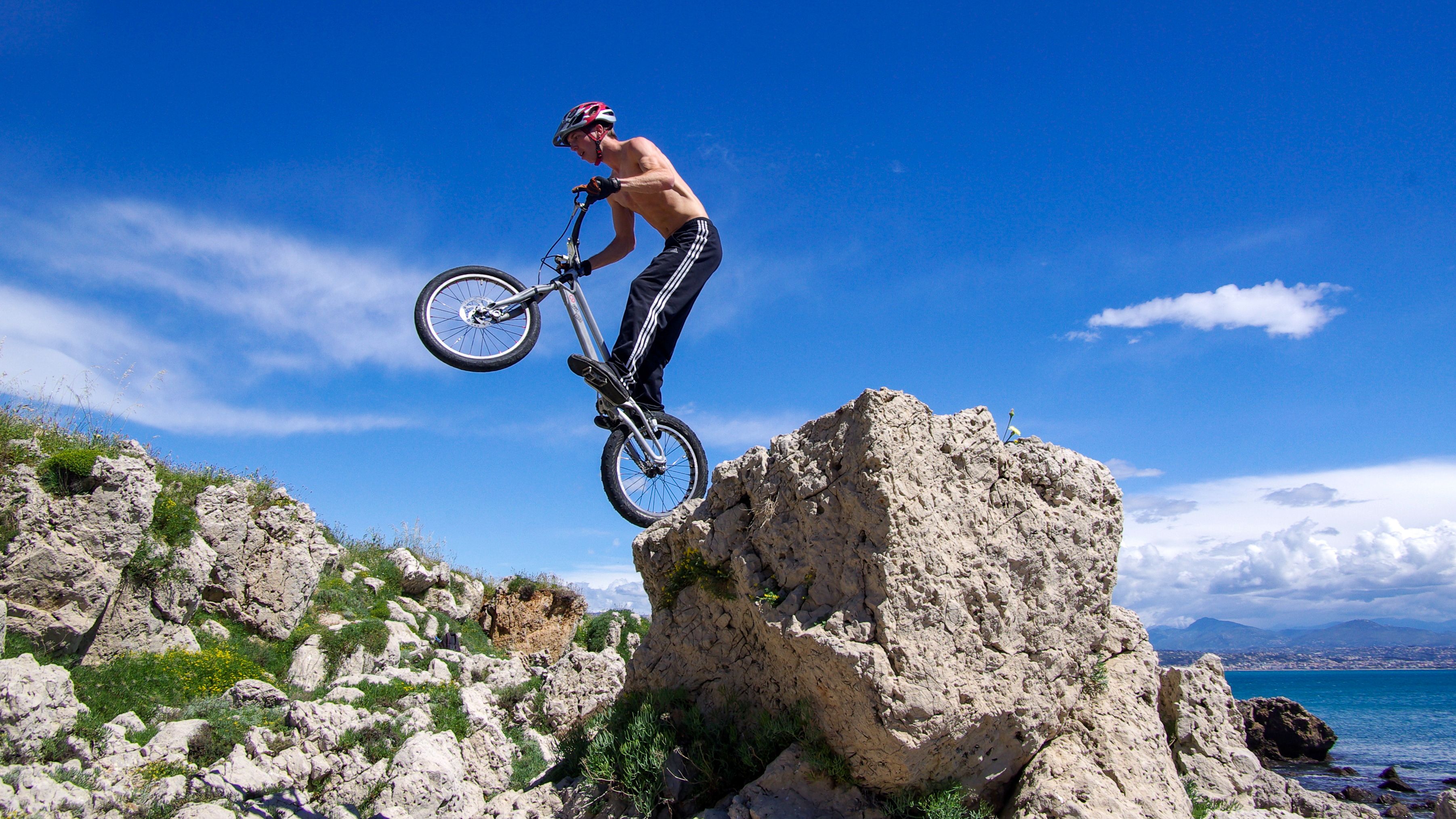 Man performing daring mountain bike stunt on rocky terrain under a clear blue sky.