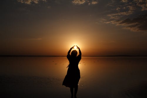 Silhouette of Woman Standing with Arms Raised at Sunset