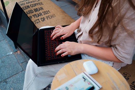 A woman with long hair typing on a laptop outdoors at a café, focusing on remote work.