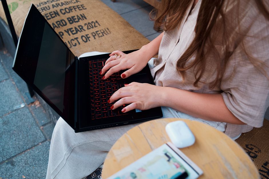 Photo by iam hogir on Pexels A woman with long hair typing on a laptop outdoors at a café, focusing on remote work.