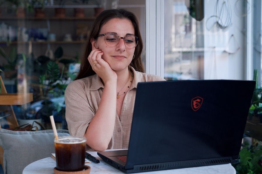 A young woman in a cafe working on her laptop, drinking iced coffee on a warm day.
