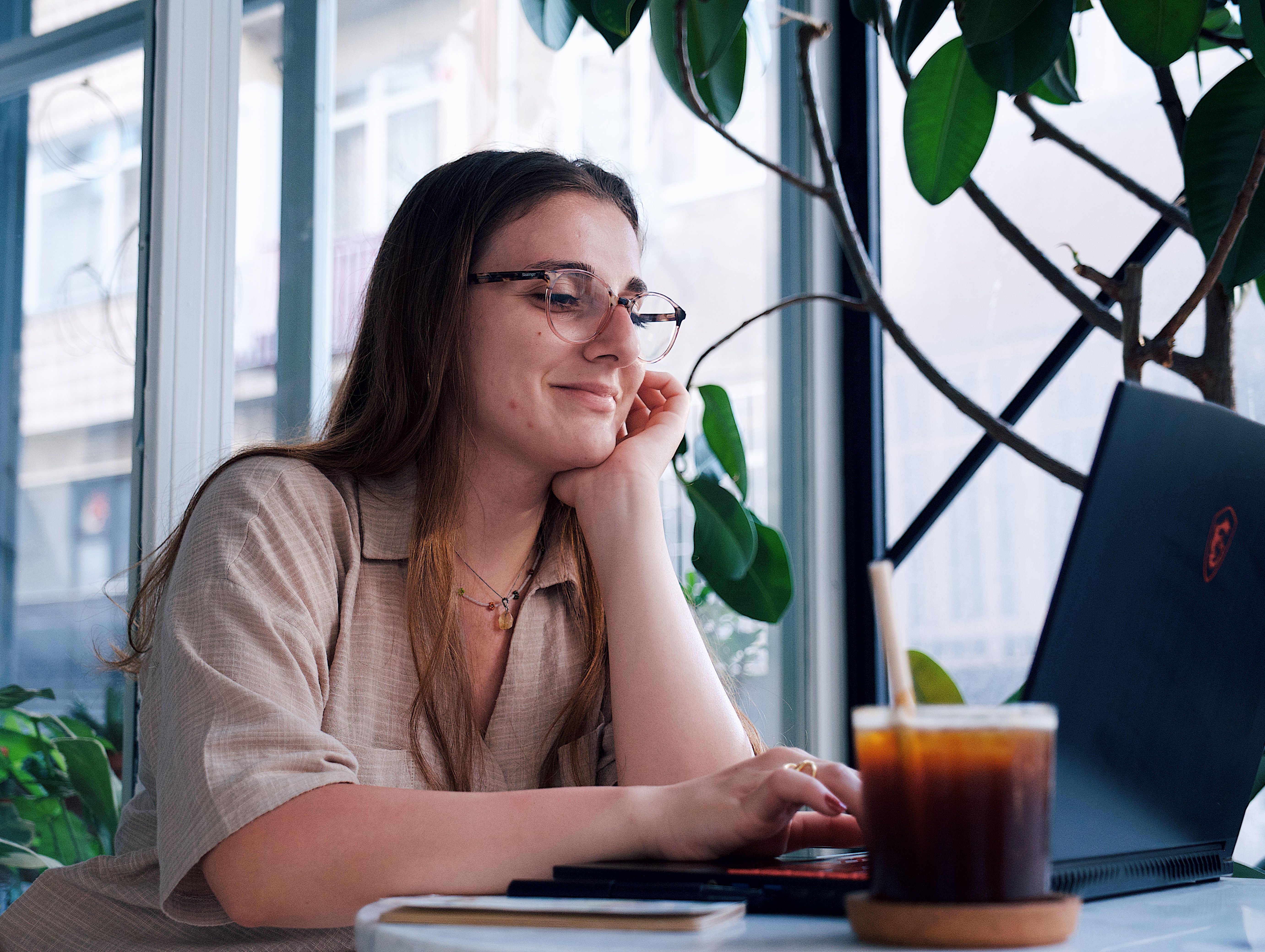 Woman enjoying coffee while working on her laptop in a bright, indoor cafe setting.