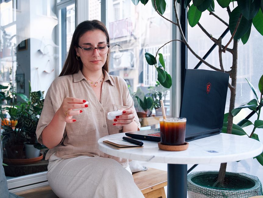 Woman enjoys coffee while working on laptop in a bright cafe.