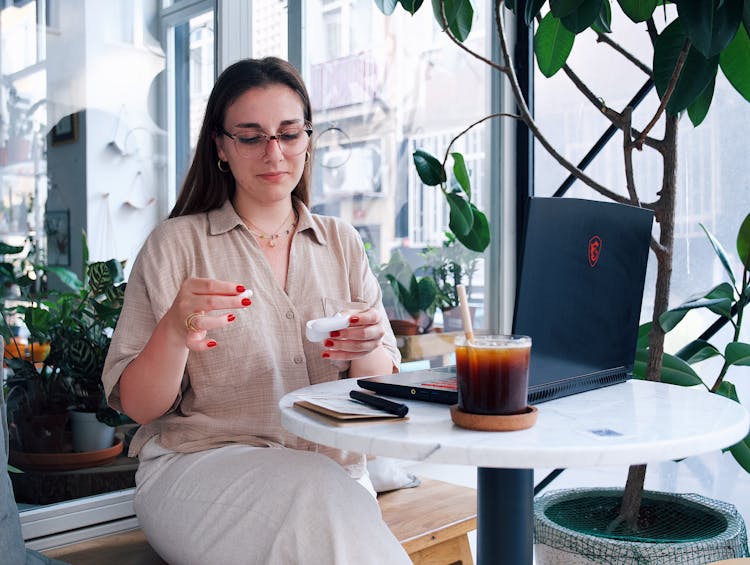 Woman In Shirt And Eyeglasses Sitting By Table With Laptop