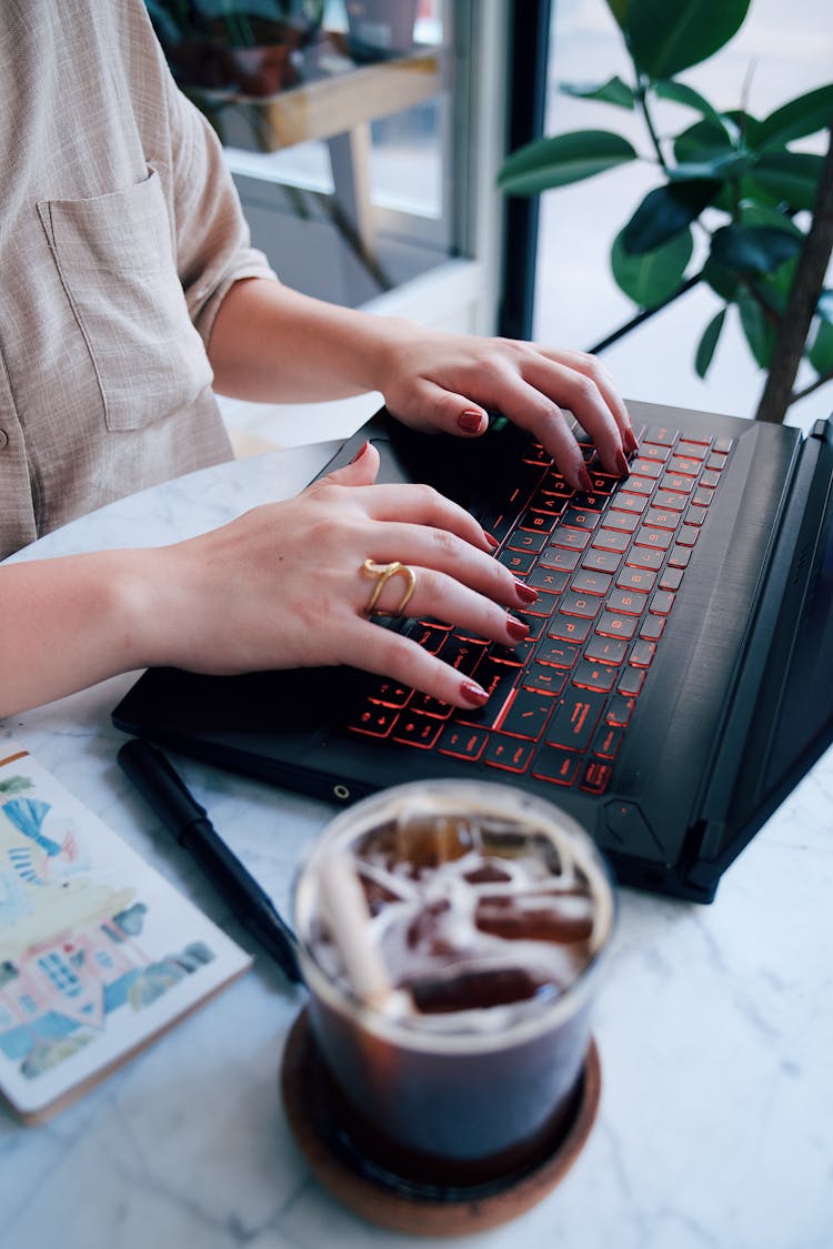 Close-up Of A Woman Sitting At The Table In A Cafe And Using A Laptop