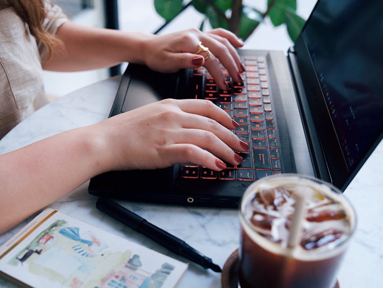 Close-up Of A Woman Sitting At The Table In A Cafe And Using A Laptop