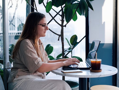 Young Woman Sitting at the Table in a Cafe and Using a Laptop