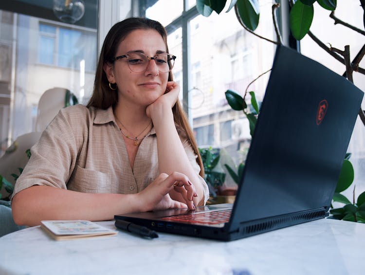 Young Woman Sitting At The Table In A Cafe And Using A Laptop