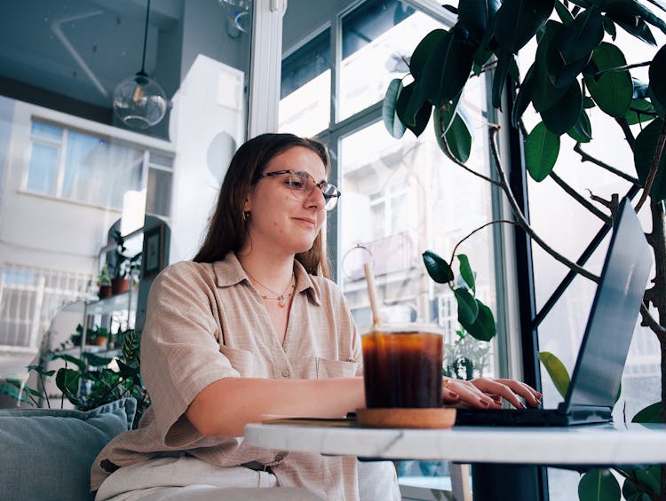 Young Woman Sitting At The Table In A Cafe And Using A Laptop