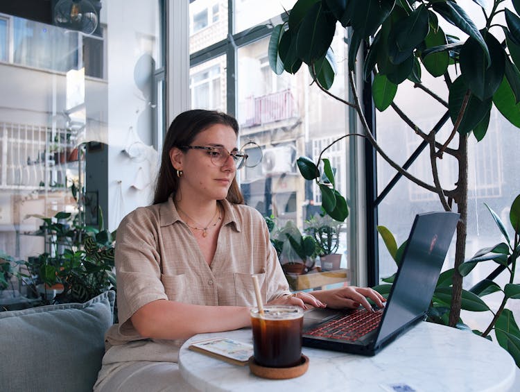 Young Woman Sitting At The Table In A Cafe And Using A Laptop