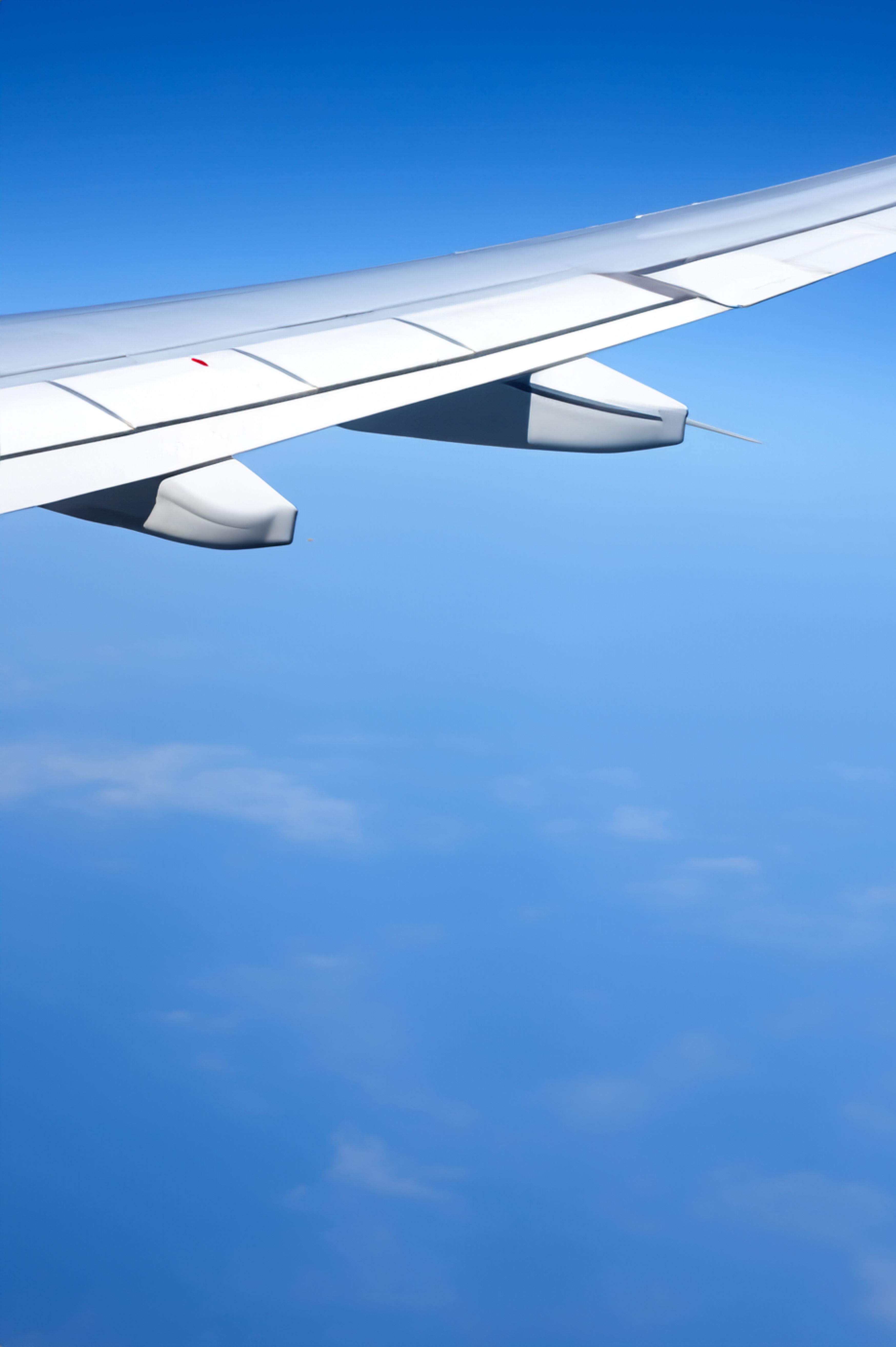 View of airplane wing against a clear blue sky from a plane window during a daytime flight.