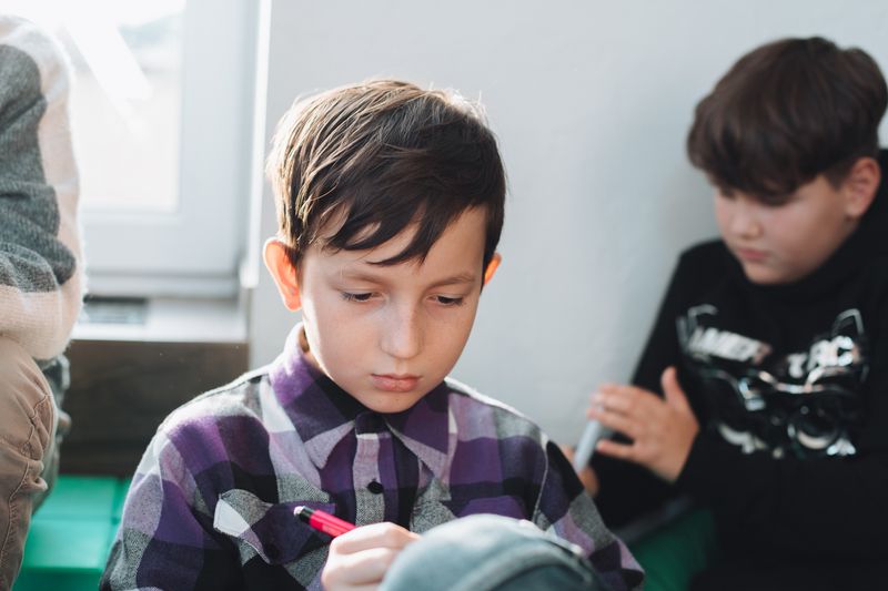 A young schoolboy concentrating while writing with a pen in a classroom setting.