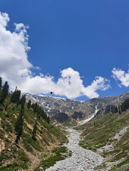 A scenic aerial view of a snowy mountain trail with a flying drone under a clear blue sky.