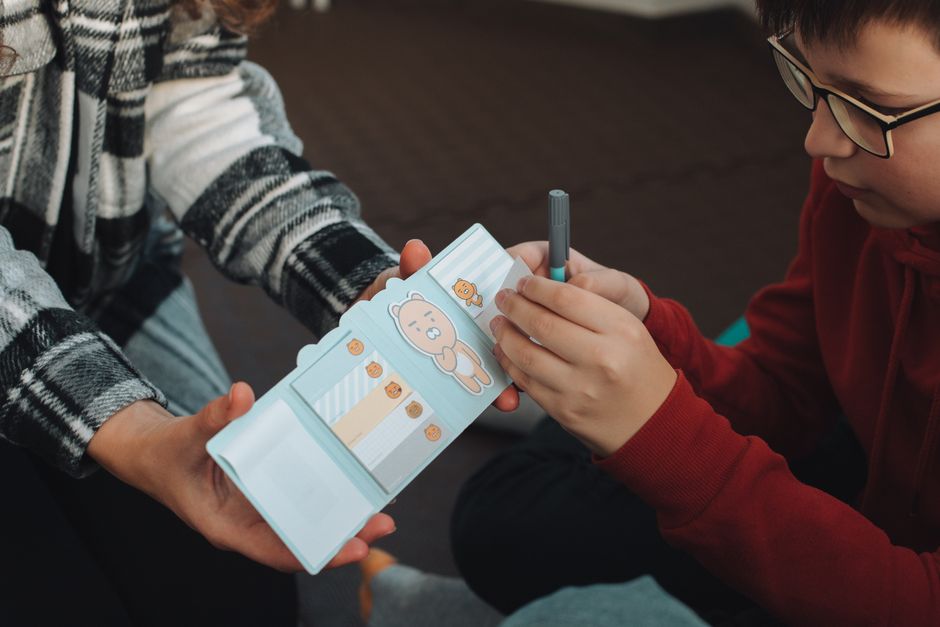 Photo by Oleskandra Biliak on Pexels A child in a red hoodie writes in a cartoon-themed notebook while an adult assists. - Photo by Oleskandra Biliak on Pexels