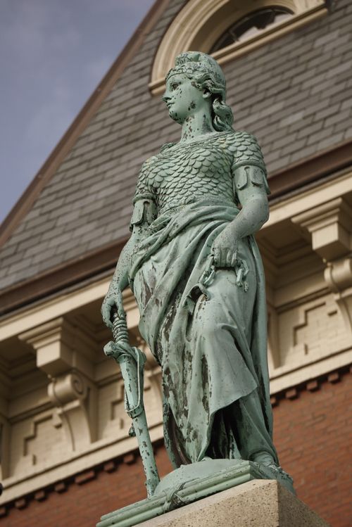 Free A vintage statue of a woman holding a sword in front of a historic building exterior. Stock Photo