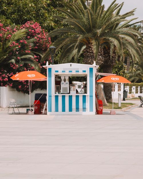 Free Quaint ice cream stand with vibrant umbrellas amidst palm trees in sunny Benidorm, Spain. Stock Photo
