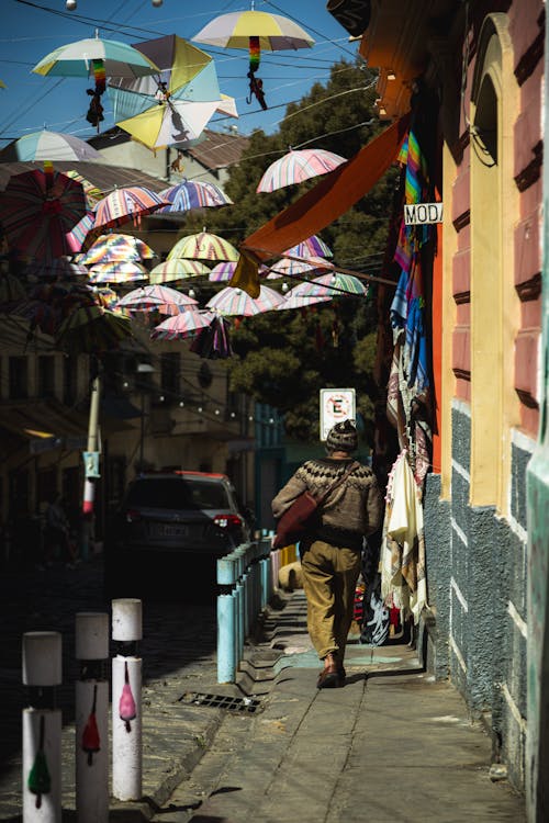 Back of a Woman Walking along the Sidewalk with Colorful Umbrellas Hanging in the Background