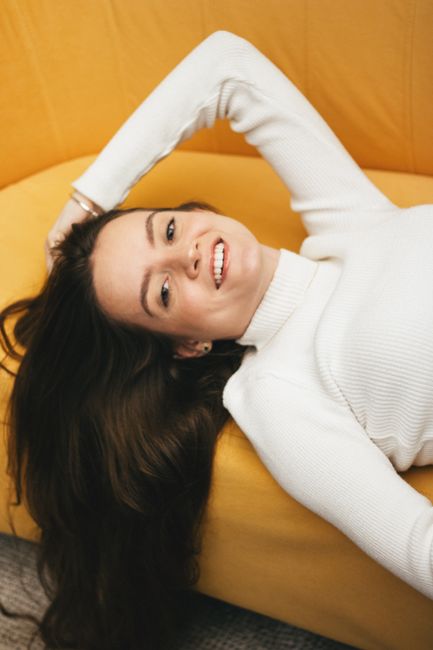 Vertical portrait of a smiling woman in a white sweater lying on a yellow couch