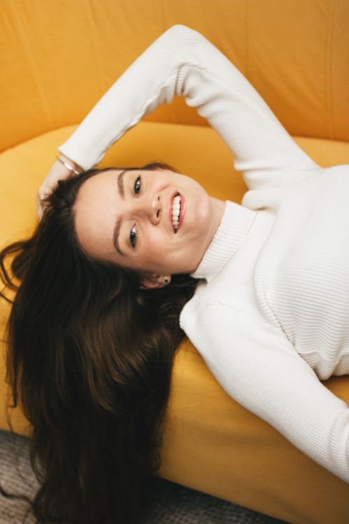 Free Vertical portrait of a smiling woman in a white sweater lying on a yellow couch Stock Photo
