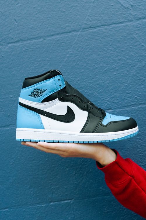 Free Hand holding a stylish black, white, and blue sneaker against a blue background. Stock Photo