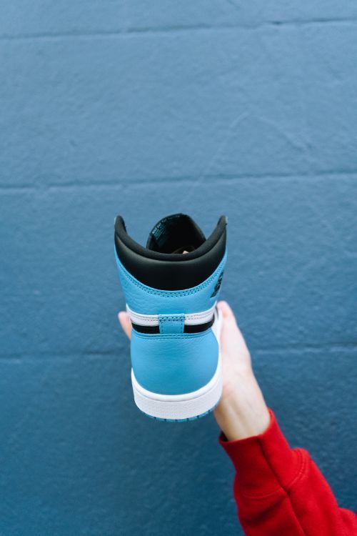 Free Person holding a blue sneaker against a blue wall, showcasing modern style. Stock Photo