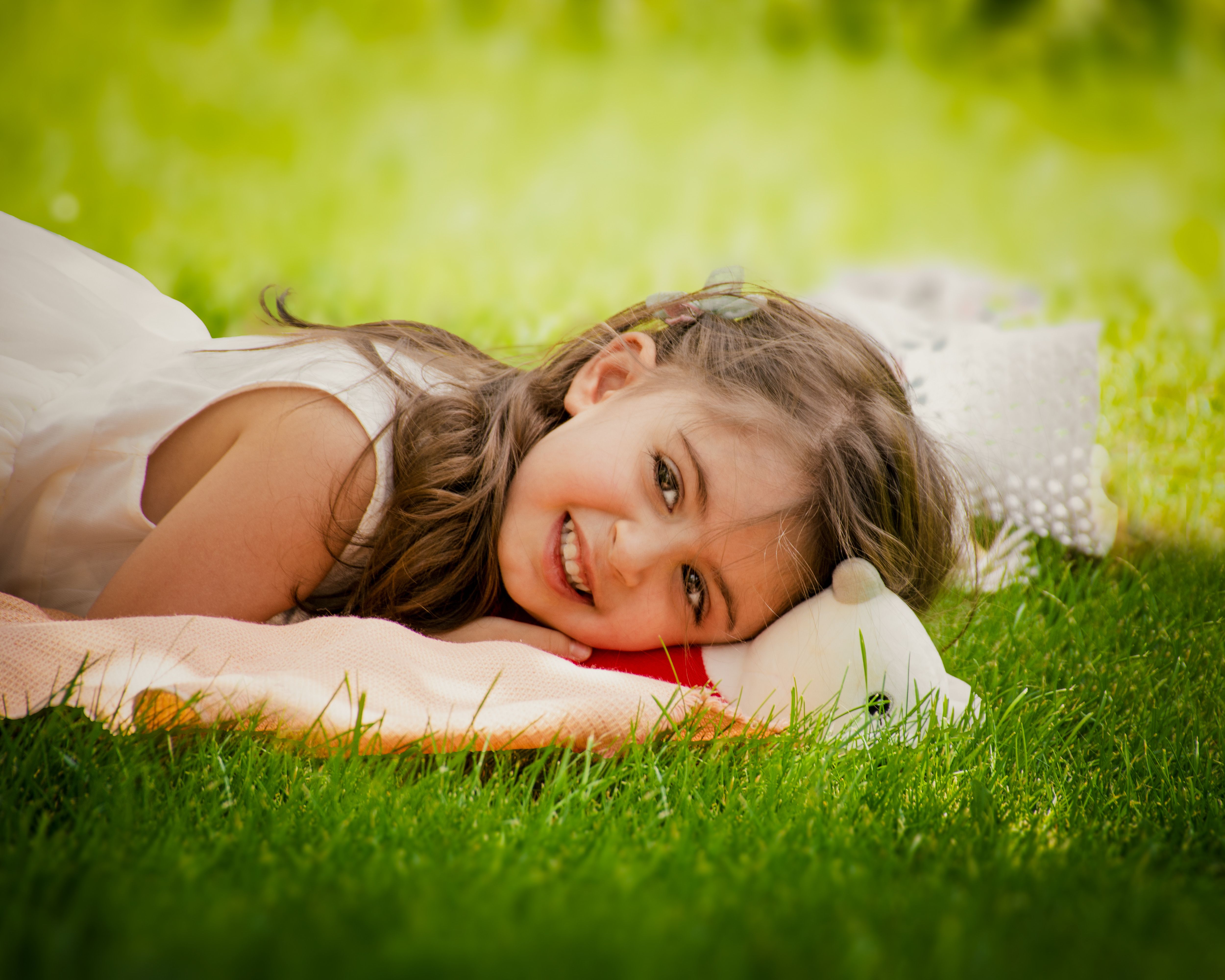 Adorable young girl lying on grass, smiling in a sunny park during summer.
