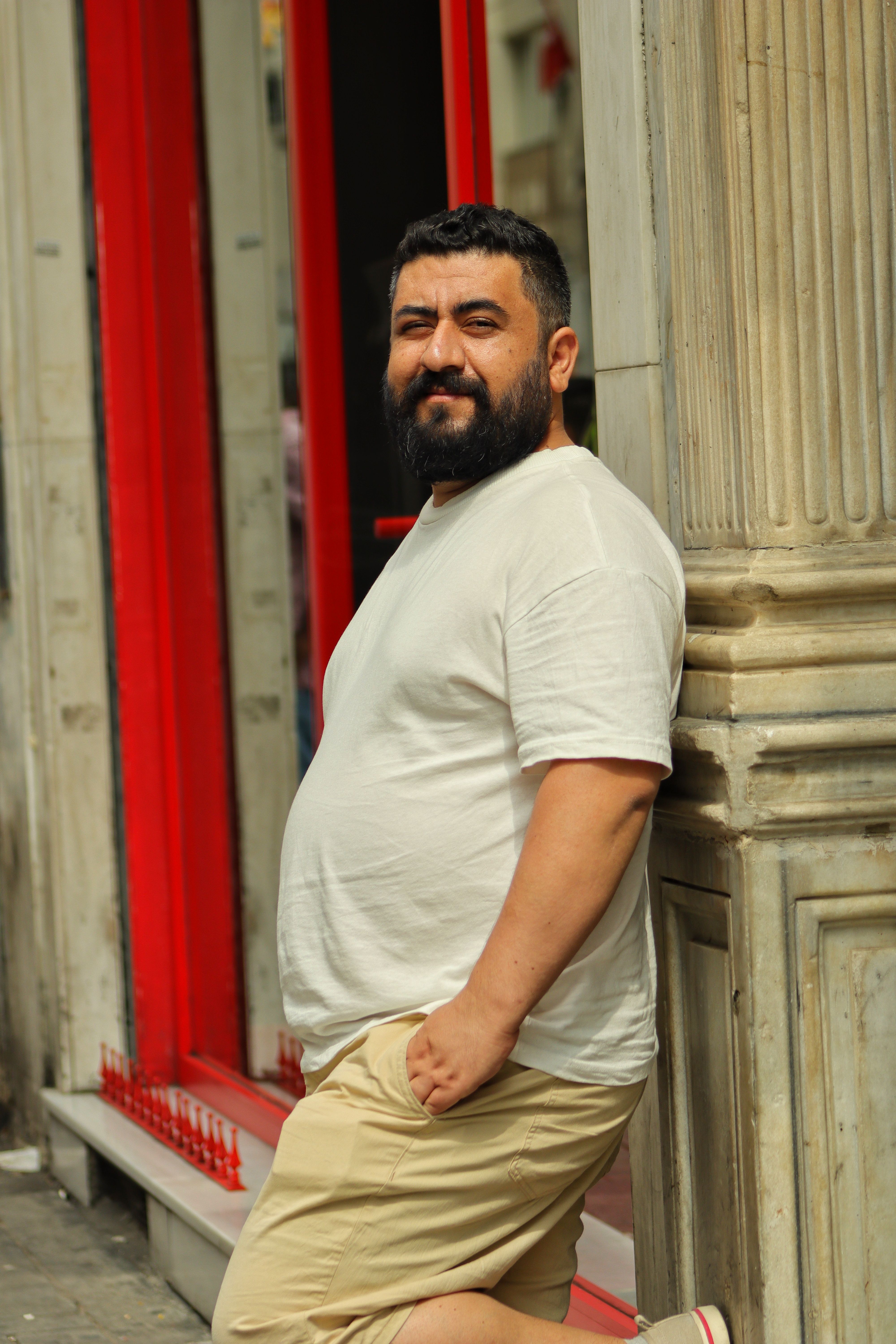 Portrait of a bearded man in casual attire leaning against a column outdoors.