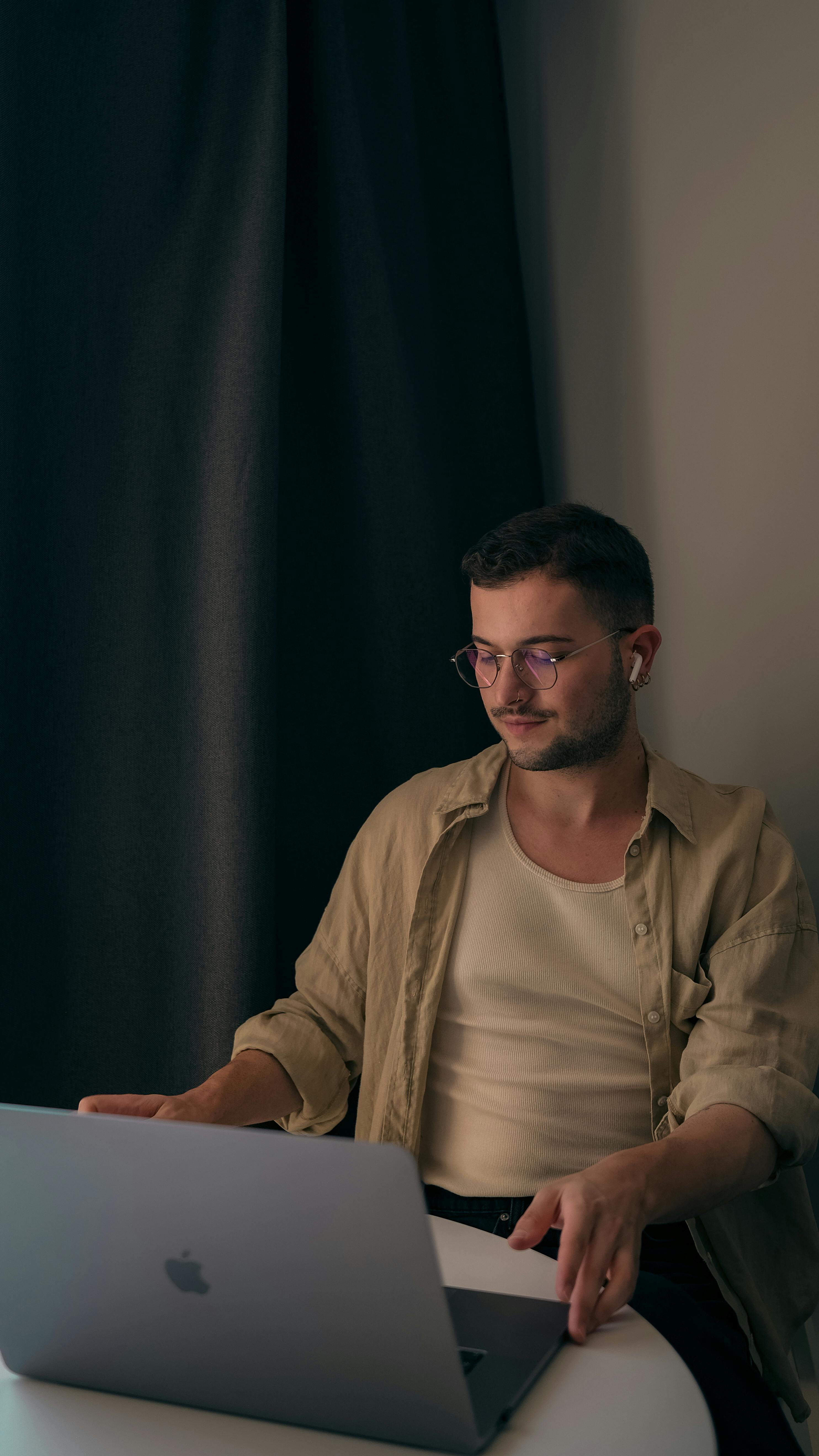 Young Caucasian man with eyeglasses working on a laptop at a table indoors.