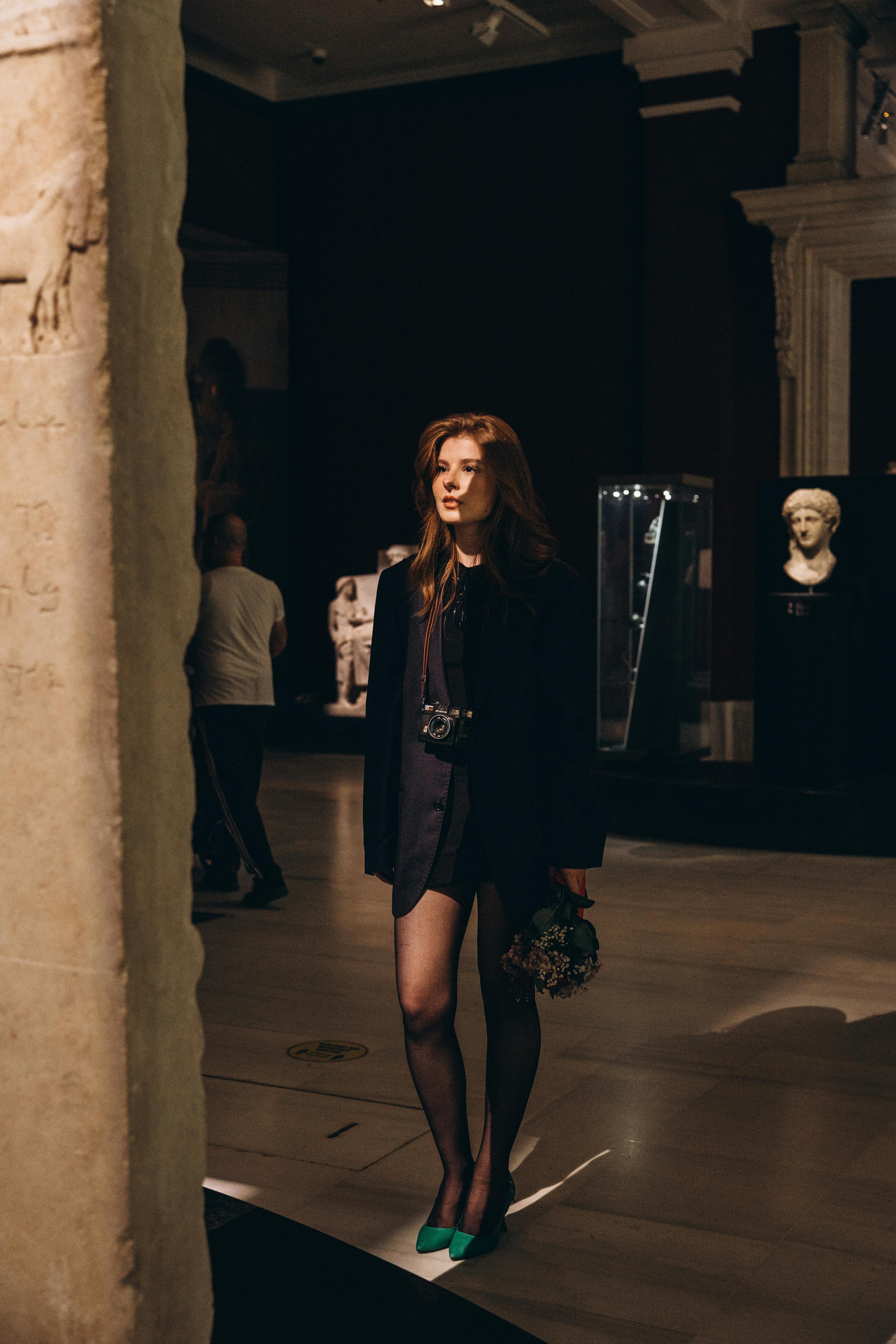 A woman in a black dress and green shoes standing in an art gallery