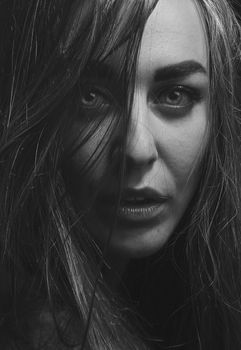 Close-up black and white portrait of a woman with tousled hair, expressing emotion.