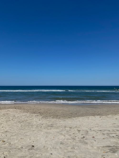 Free A tranquil sunny beach with gentle waves under a vibrant blue sky. Perfect summer getaway. Stock Photo