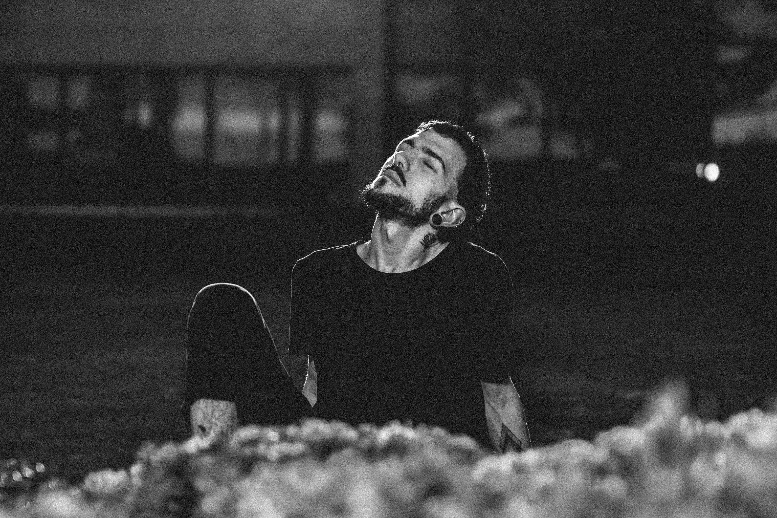 A serene monochrome portrait of a man with beard and short hair sitting outside at night.