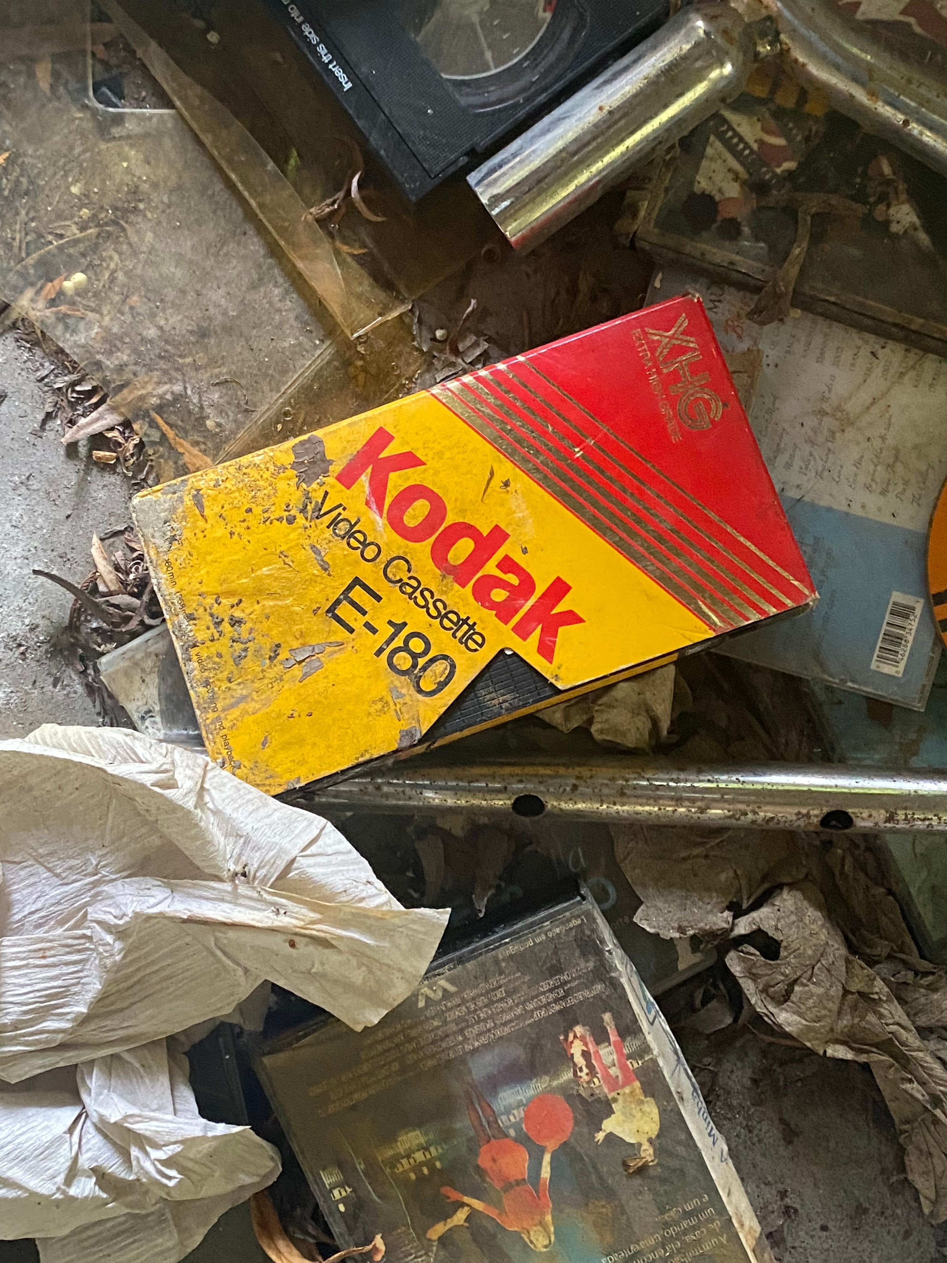 An old Kodak video cassette amidst a pile of dusty, discarded items.