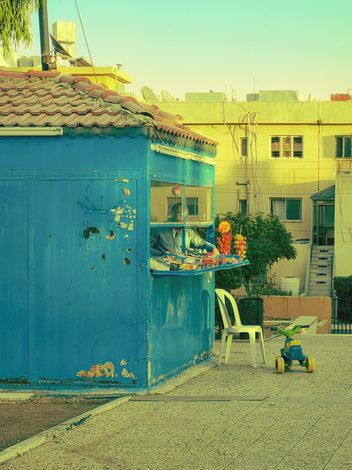 Free A vibrant urban scene featuring a street vendor kiosk with a blue exterior, toys nearby, and city buildings in the background. Stock Photo