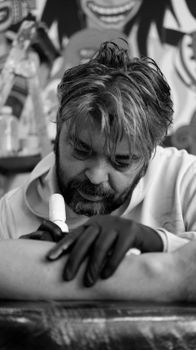 Monochrome photo of a tattoo artist working in a studio, wearing gloves and focusing intensely.